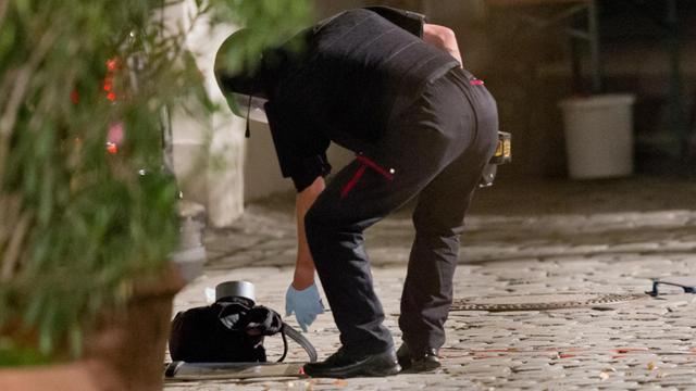 Ein Polizist bückt sich, um einen Rucksack aufzuheben.