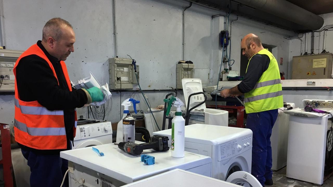 Zwei Mitarbeiter von Envie beim Reparieren in der Werkstatt. Zwei Mitarbeiter von Envie beim Reparieren in der Werkstatt.