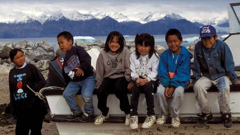 Inuit-Kinder sitzen in einer Reihe auf dem Rad eines Motorbootes in Nunavut.