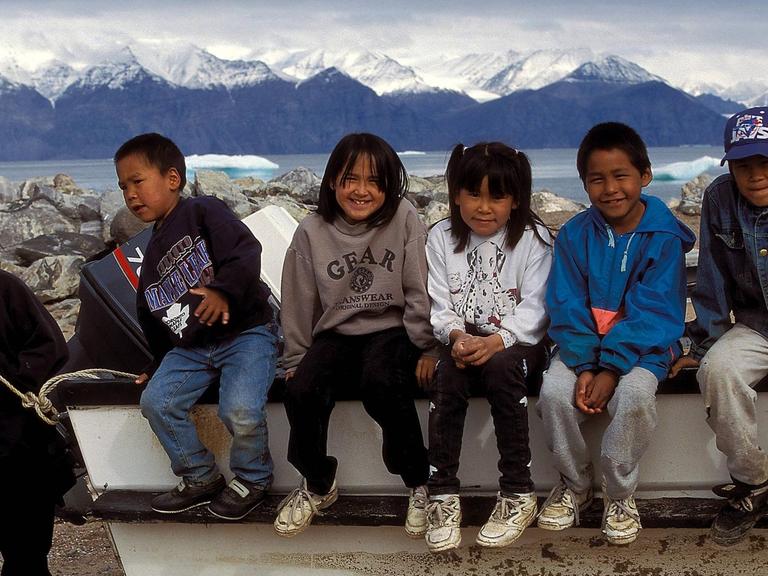 Inuit-Kinder sitzen in einer Reihe auf dem Rad eines Motorbootes in Nunavut.