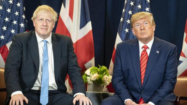 Links sitzt Boris Johnson, rechts Donald Trump vor ihren jeweiligen Landes-Flaggen
