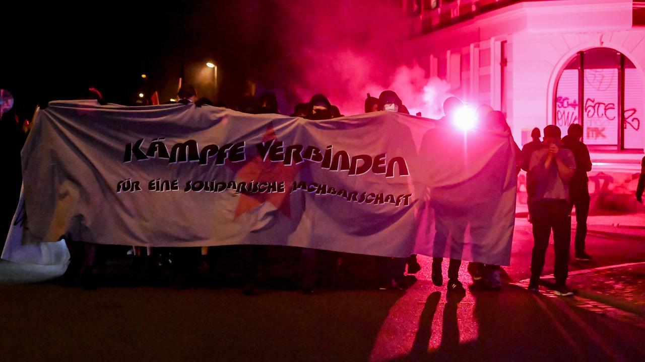 Teilnehmende einer Demonstration ziehen mit roten Pyro-Fackeln und einem Banner, auf dem steht "für eine solidarische Nachbarschaft", durch den Stadtteil Connewitz in Leipzig.