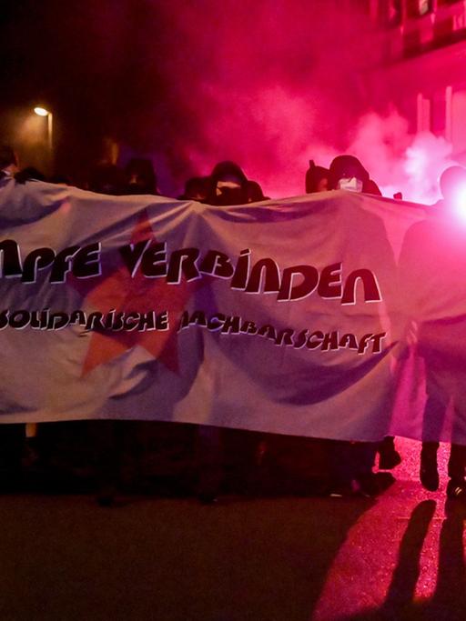 Teilnehmende einer Demonstration ziehen mit roten Pyro-Fackeln und einem Banner, auf dem steht "für eine solidarische Nachbarschaft", durch den Stadtteil Connewitz in Leipzig.