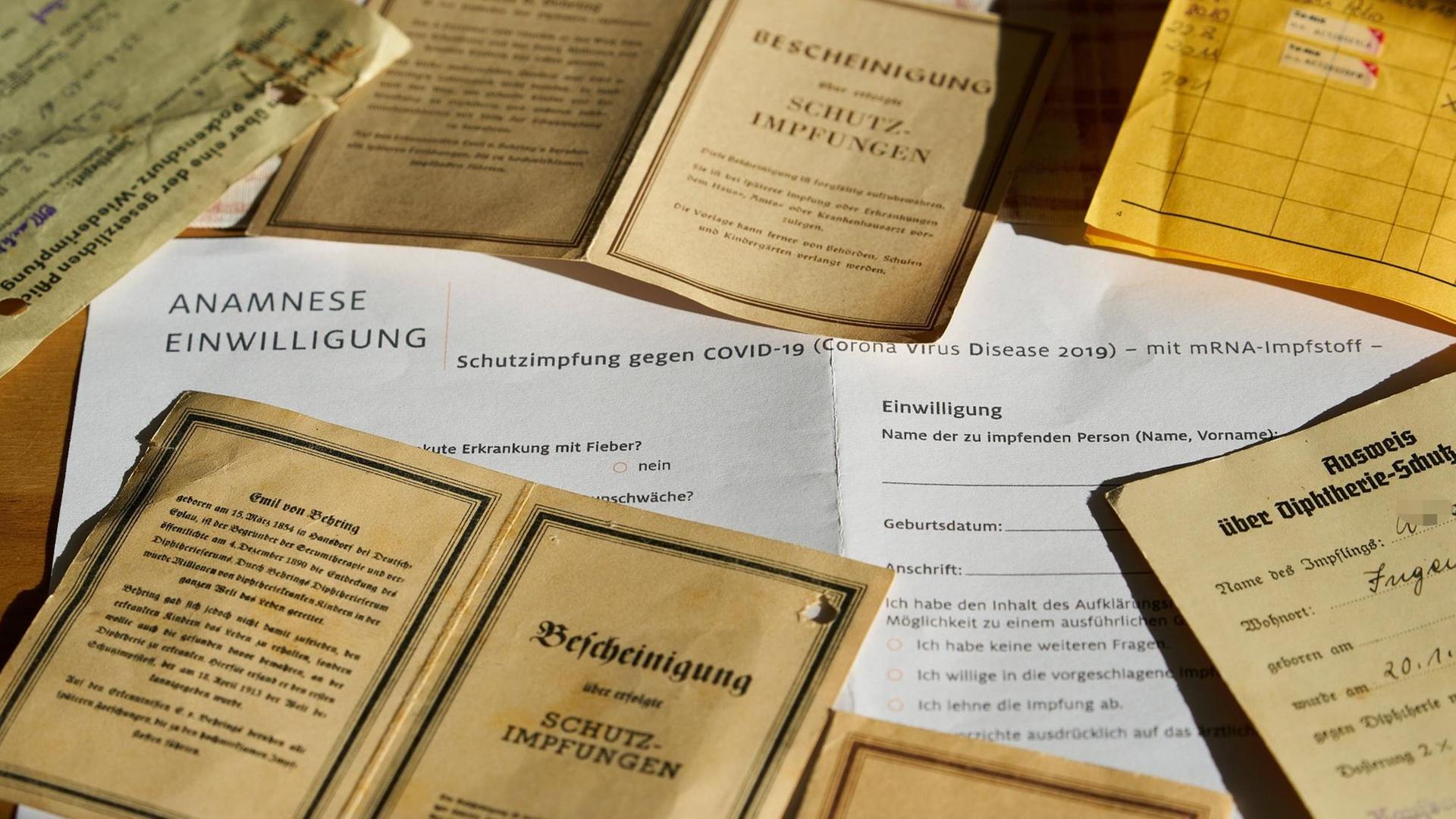 Ein Formular zur Corona-Impfung sowie alte Impfbücher und -bescheinigungen liegen unordentlich auf einem Haufen. Ein Formular zur Corona-Impfung sowie alte Impfbücher und -bescheinigungen liegen unordentlich auf einem Haufen.