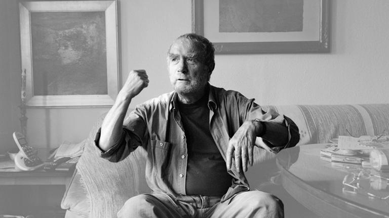 Der Buchgestalter Lothar Reher sitzt in seinem Wohnzimmer auf dem Sofa und stützt einen Ellbogen auf einem Couchtisch auf. Der Buchgestalter Lothar Reher sitzt in seinem Wohnzimmer auf dem Sofa und stützt einen Ellbogen auf einem Couchtisch auf.