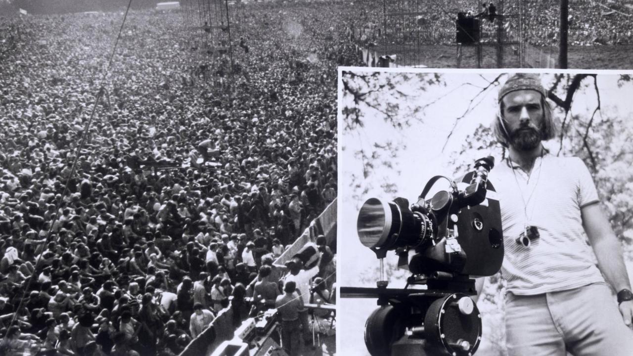 Regisseur Michael Wadleigh mit einer Filmkamera, im Hintergrund das Publikum des Woodstock-Musikfestivals