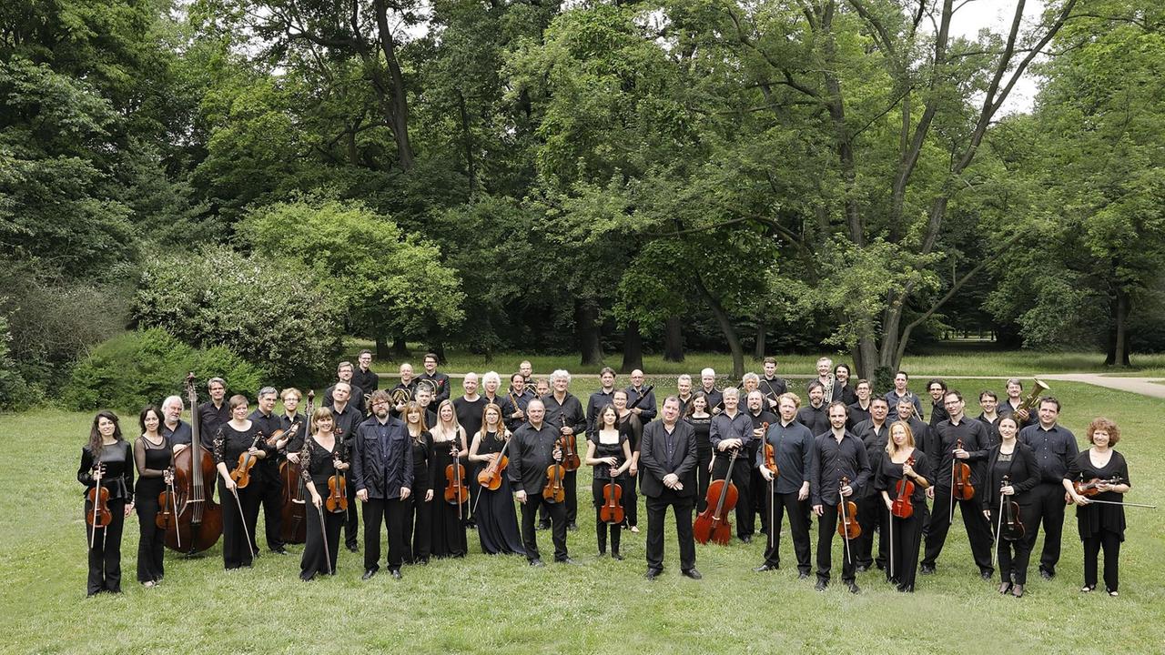 Das Orchester steht auf einer große Wiese, die von Bäumen gesäumt ist. Das Orchester steht auf einer große Wiese, die von Bäumen gesäumt ist.