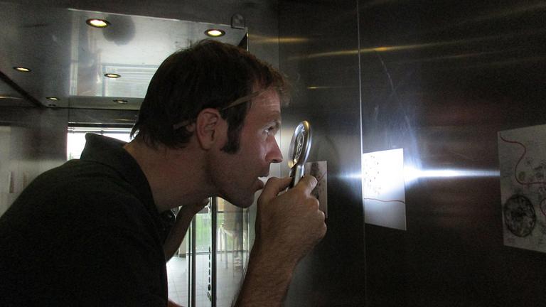 Ein Mann betrachtet mit einer Lupe Bilder im Kunstlift Hamburg.