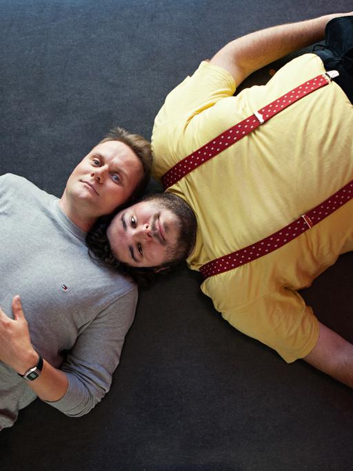 Devid Striesow und Axel Ranisch liegen auf dem Boden, die Köpfe nebeneinander