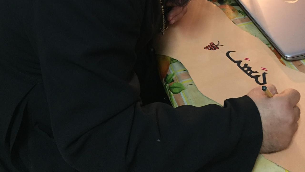 Dayroyo Boulus sitzt an einem Tisch und beschreibt ein Lederstück mit dickem Filzstift auf Aramäisch Dayroyo Boulus sitzt an einem Tisch und beschreibt ein Lederstück mit dickem Filzstift auf Aramäisch