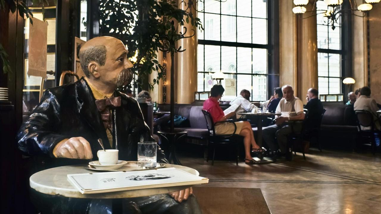 Eine Figur des österreichischen Schriftstellers Peter Altenberg sitzt mit einer Zeitung und einer Kaffeetasse an einem kleinen, runden Tisch im Wiener Café Central. Eine Figur des österreichischen Schriftstellers Peter Altenberg sitzt mit einer Zeitung und einer Kaffeetasse an einem kleinen, runden Tisch im Wiener Café Central.