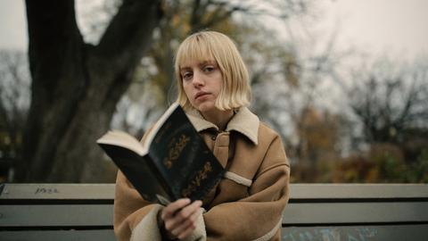 Eine junge Frau sitzt auf einer Parkbank und liest ein Buch.