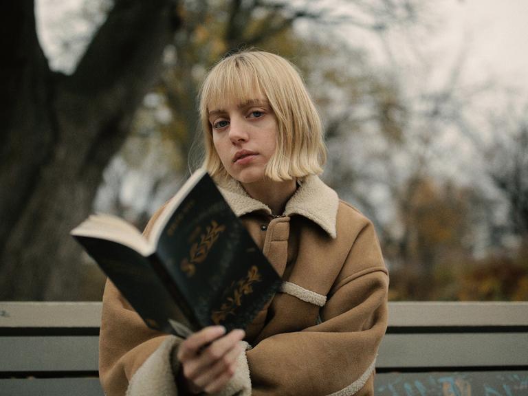 Eine junge Frau sitzt auf einer Parkbank und liest ein Buch.
