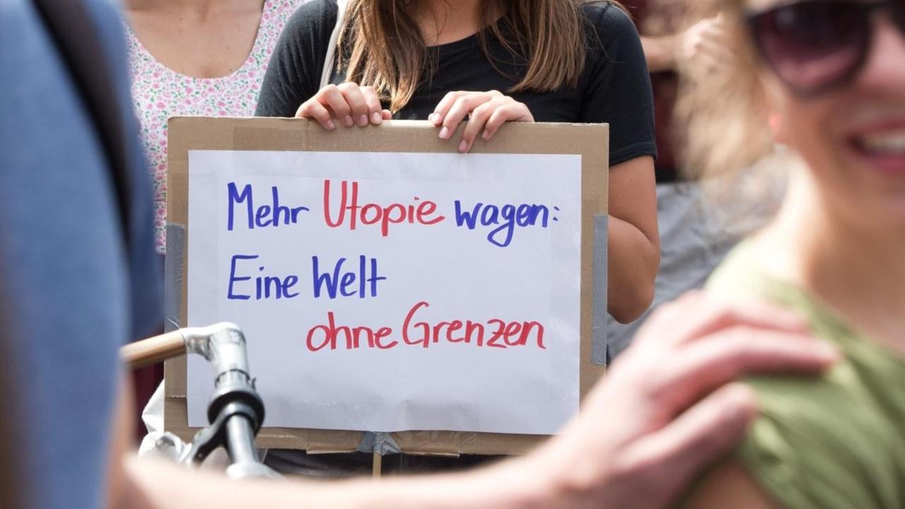 Eine Demonstrantin in Berlin-Kreuzberg hält bei Protesten für ein Bleiberecht für Flüchtlinge ein Schild mit der Aufschrift "Mehr Utopie wagen: Eine Welt ohne Grenzen". (5.7.2014) Eine Demonstrantin in Berlin-Kreuzberg hält bei Protesten für ein Bleiberecht für Flüchtlinge ein Schild mit der Aufschrift "Mehr Utopie wagen: Eine Welt ohne Grenzen". (5.7.2014)