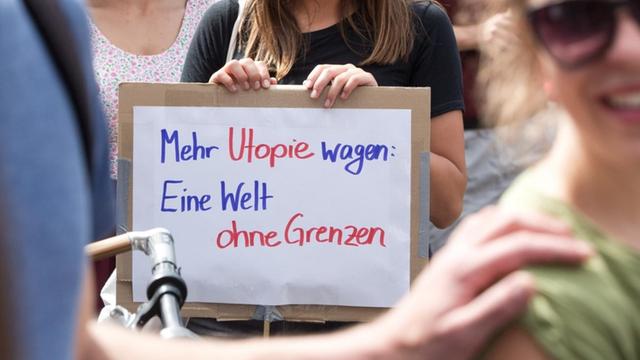 Eine Demonstrantin in Berlin-Kreuzberg hält bei Protesten für ein Bleiberecht für Flüchtlinge ein Schild mit der Aufschrift "Mehr Utopie wagen: Eine Welt ohne Grenzen". (5.7.2014)
