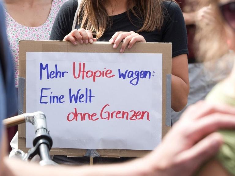 Eine Demonstrantin hält bei Protesten für ein Bleiberecht für Flüchtlinge ein Schild mit der Aufschrift "Mehr Utopie wagen: Eine Welt ohne Grenzen".