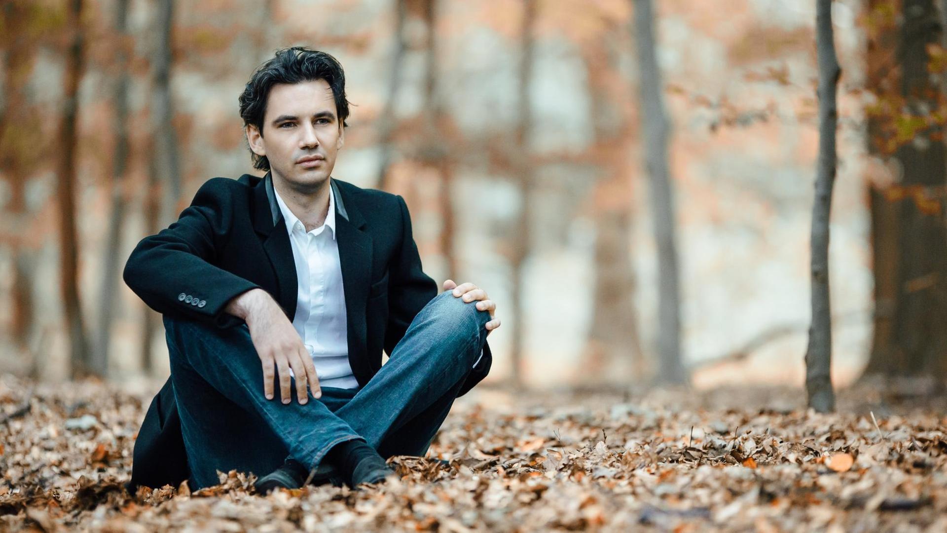 Ein junger Mann sitzt mit überkreuzten Beinen in einem herbstlichen Wald. Ein junger Mann sitzt mit überkreuzten Beinen in einem herbstlichen Wald.