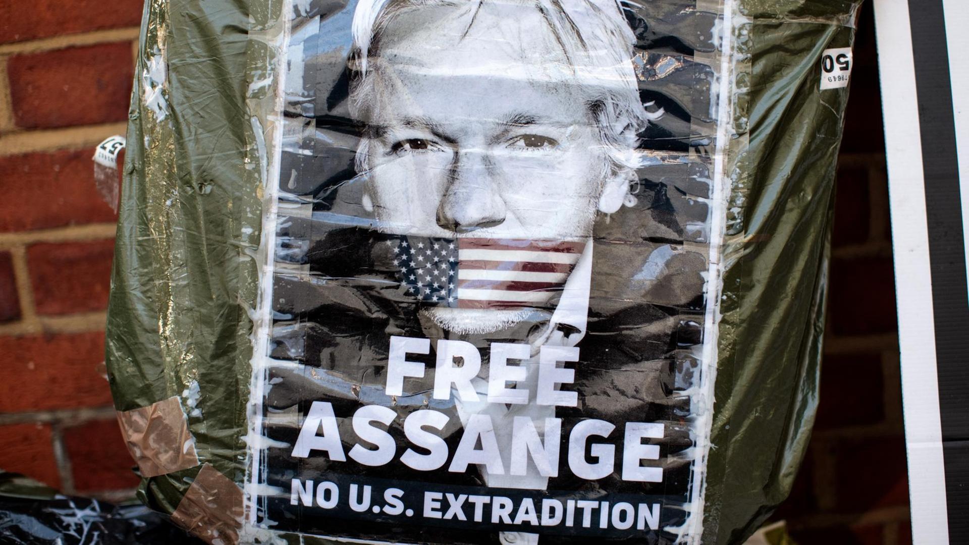 Plakat mit einem Porträt von Julian Assange mit der amerikanischen Fahne als Knebel über seinem Mund. Protestschild vor der ecuadoranischen Botschaft in London von April 2019.