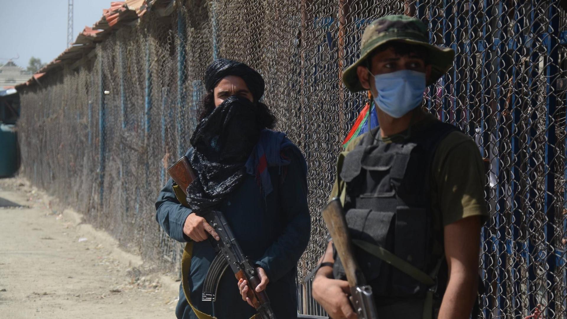 Ein Talibankämpfer und ein pakistanischer Soldat, beide bewaffnet, stehen am Grenzzaun zwischen Afghanistan und Pakistan.