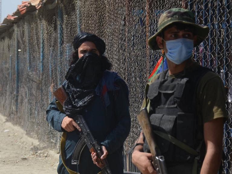 Ein Talibankämpfer und ein pakistanischer Soldat, beide bewaffnet, stehen am Grenzzaun zwischen Afghanistan und Pakistan.