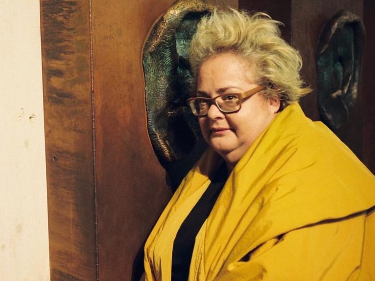 Die Komponistin lauscht an einem großen bronzenen Ohr in einer Ausstellung.