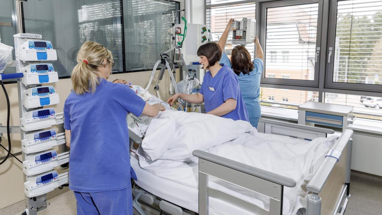 Drei Krankenschwestern stehen bei einem Patienten an einem Bett im Krankenzimmer mit Geräten der Intensivmedizin. Drei Krankenschwestern stehen bei einem Patienten an einem Bett im Krankenzimmer mit Geräten der Intensivmedizin.