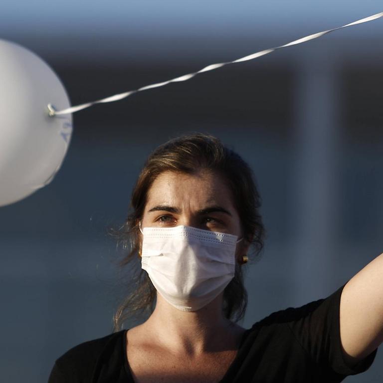 Eine Frau hält einen weißen Luftballon auf einer Corona-Gedenkveranstaltung in Brasilia, Brasilien, in die Luft