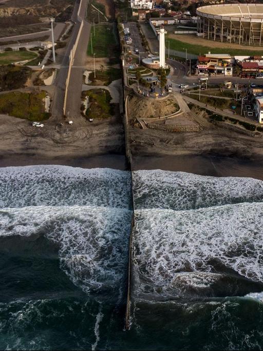 Luftansicht des Grenzzauns zwischen den USA und Mexiko, der durch den Strand bis mitten hinein ins Wasser reicht.