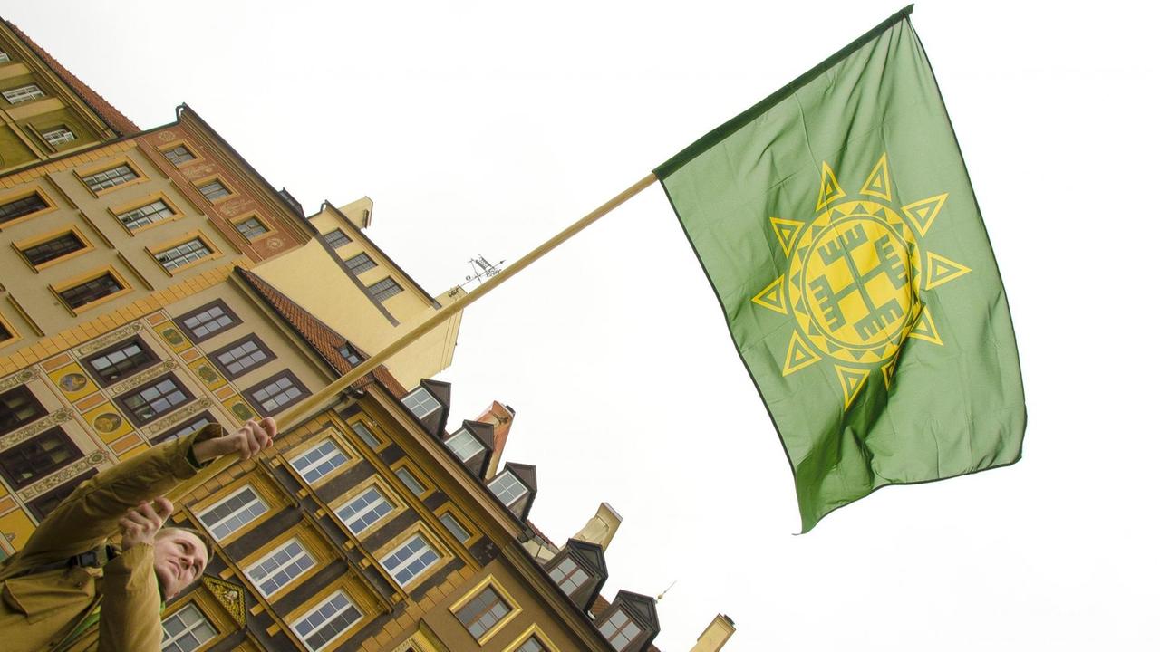 Mann schwingt Fahne: grüner Hintergrund mit gelben Runensymbol