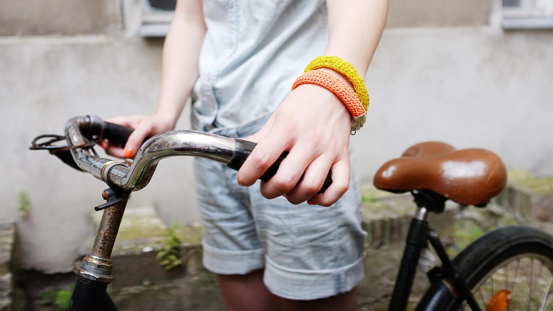 Detail eines Fahrradlenkers der von einer Frau gehalten wird. Sie trägt ein oranges und ein gelbes Armband und rote Fingernägel. Detail eines Fahrradlenkers der von einer Frau gehalten wird. Sie trägt ein oranges und ein gelbes Armband und rote Fingernägel.