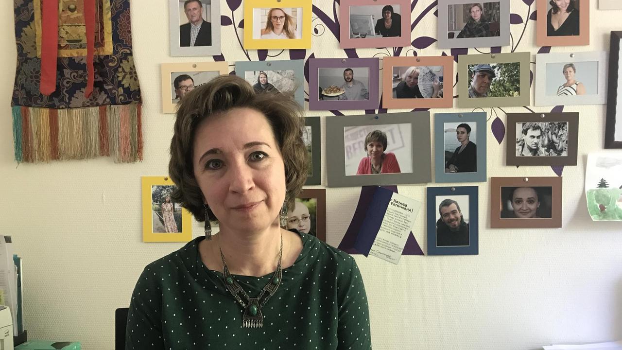 Frau im Büro vor einer Wand mit Fotos sitzend Frau im Büro vor einer Wand mit Fotos sitzend