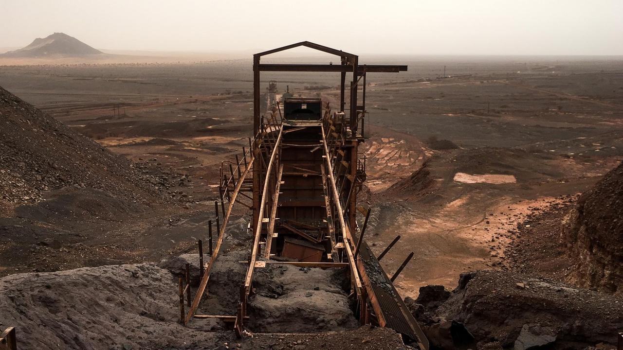 Seit Jahrhunderten wird hier am Kedia D'Idjil Eisen abgebaut. Die industrielle Förderung begann allerdings erst nach der Unabhängigkeit Mauretaniens in den 1960er-Jahren. Am Horizont begegnen sich der schwarze Fels des Eisengebirges und der rötlich-gelbe Sand der Sahara.