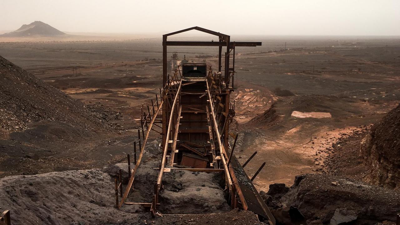 Seit Jahrhunderten wird hier am Kedia D'Idjil Eisen abgebaut. Die industrielle Förderung begann allerdings erst nach der Unabhängigkeit Mauretaniens in den 1960er-Jahren. Am Horizont begegnen sich der schwarze Fels des Eisengebirges und der rötlich-gelbe Sand der Sahara. Seit Jahrhunderten wird hier am Kedia D'Idjil Eisen abgebaut. Die industrielle Förderung begann allerdings erst nach der Unabhängigkeit Mauretaniens in den 1960er-Jahren. Am Horizont begegnen sich der schwarze Fels des Eisengebirges und der rötlich-gelbe Sand der Sahara.