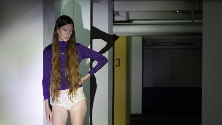 Eine Frau mit langen Haaren, lila Pullover, ohne Hose in einer Tiefgarage. Eine Frau mit langen Haaren, lila Pullover, ohne Hose in einer Tiefgarage.