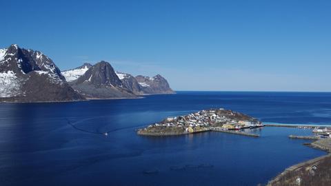 Ein auf einer Insel gelegenes Fischerdorf in Norwegen. Im Hintergrund sind Berge und der Horizont zu sehen.