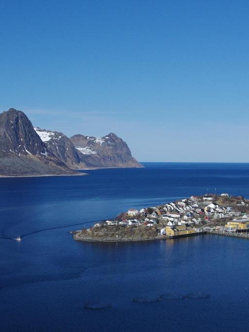 Ein auf einer Insel gelegenes Fischerdorf in Norwegen. Im Hintergrund sind Berge und der Horizont zu sehen.
