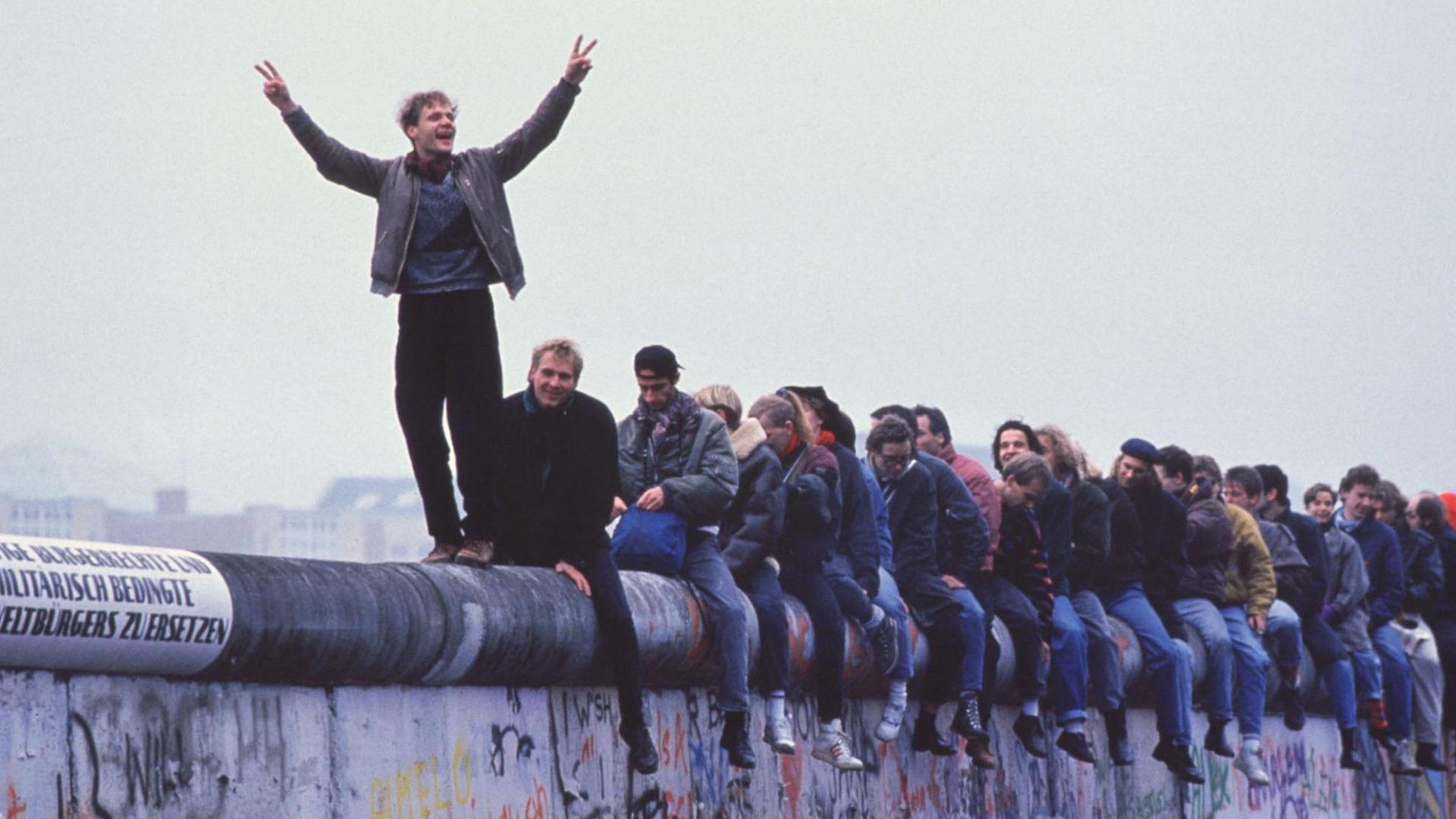 Westdeutsche sitzen am 27.9.1999 auf der Berliner Mauer und feiern die Grenzöffnung.