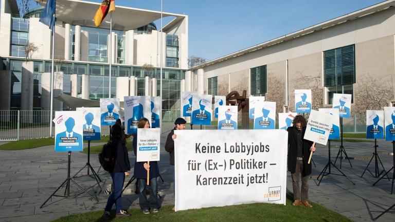 Mehrere Menschen stellen vor dem Kanzleramt zahlreiche Plakate auf Metallständer. Auf einem Transparent steht: "Keine Lobbyjobs für (Ex-) Politiker - Karenzzeit jetzt!"