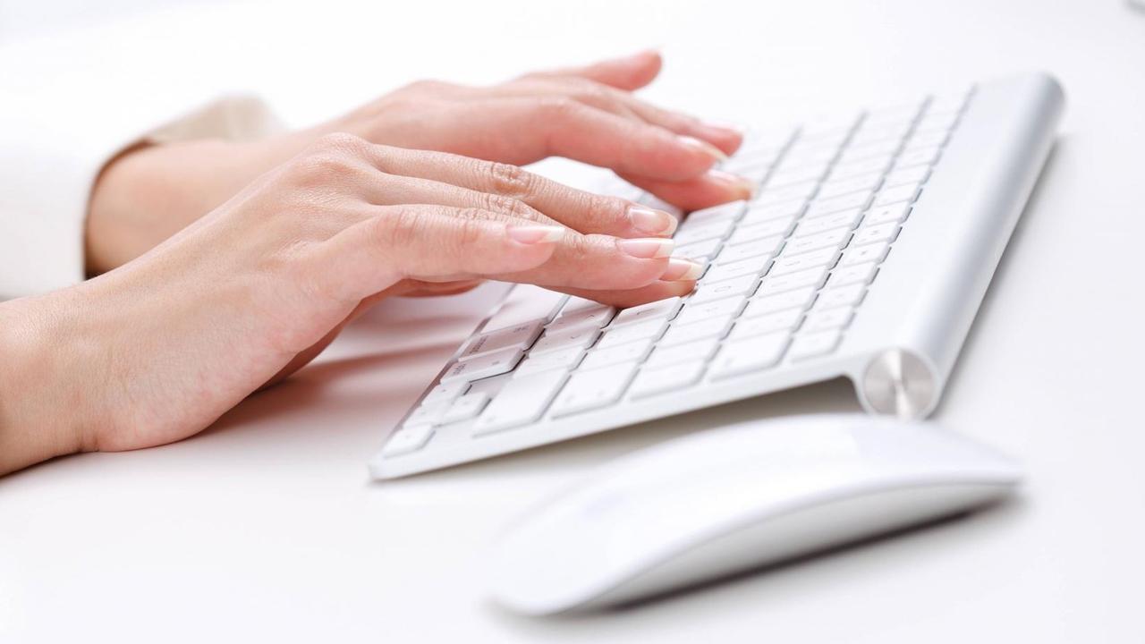 Frauenhände tippen auf einer weißen Computertastatur. Rechts daneben liegt eine weiße Computermaus. Frauenhände tippen auf einer weißen Computertastatur. Rechts daneben liegt eine weiße Computermaus.