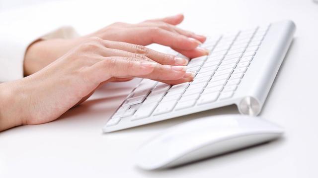 Frauenhände tippen auf einer weißen Computertastatur. Rechts daneben liegt eine weiße Computermaus.