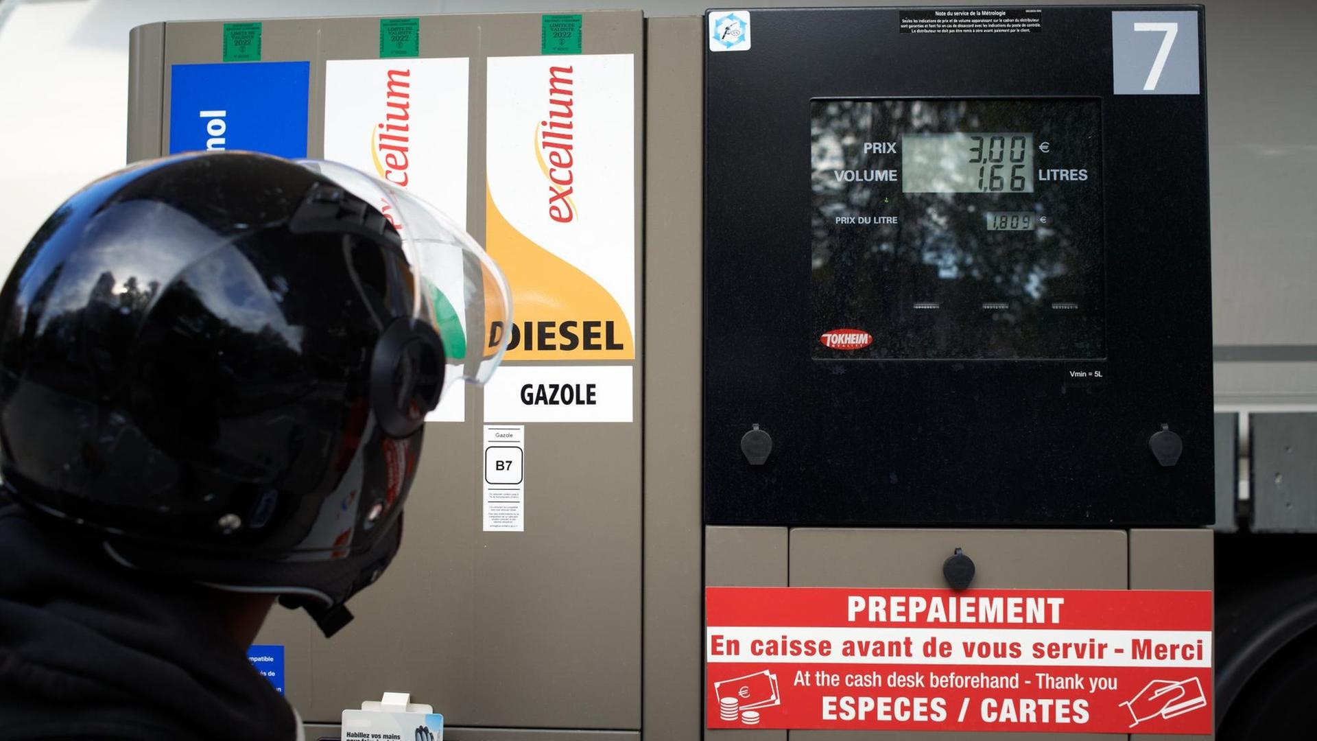 Mann mit Motorradhelm blickt auf Zapfsäule Mann mit Motorradhelm blickt auf Zapfsäule