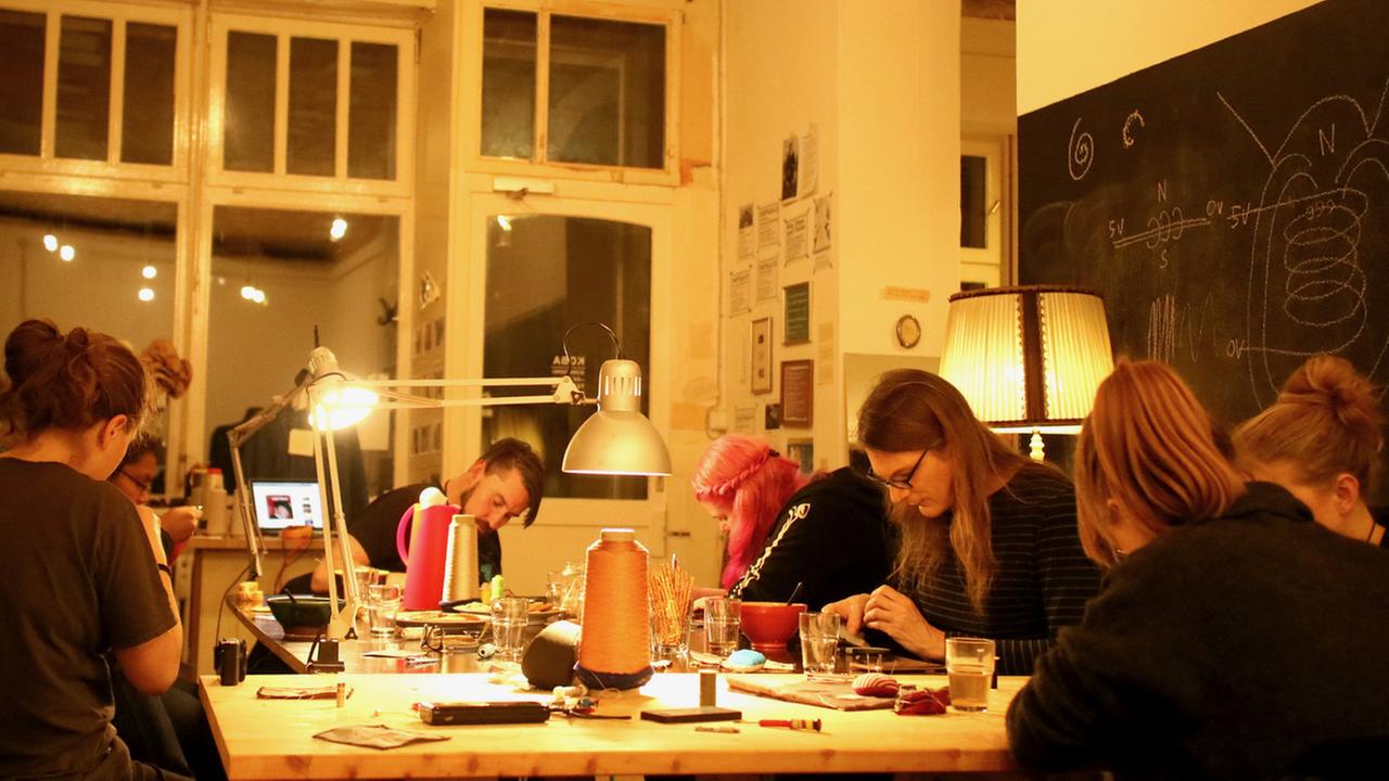 Mehrere Teilnehmer eines workshops nähen konzentriert an einem großen Werkstatt-Tisch Mehrere Teilnehmer eines workshops nähen konzentriert an einem großen Werkstatt-Tisch