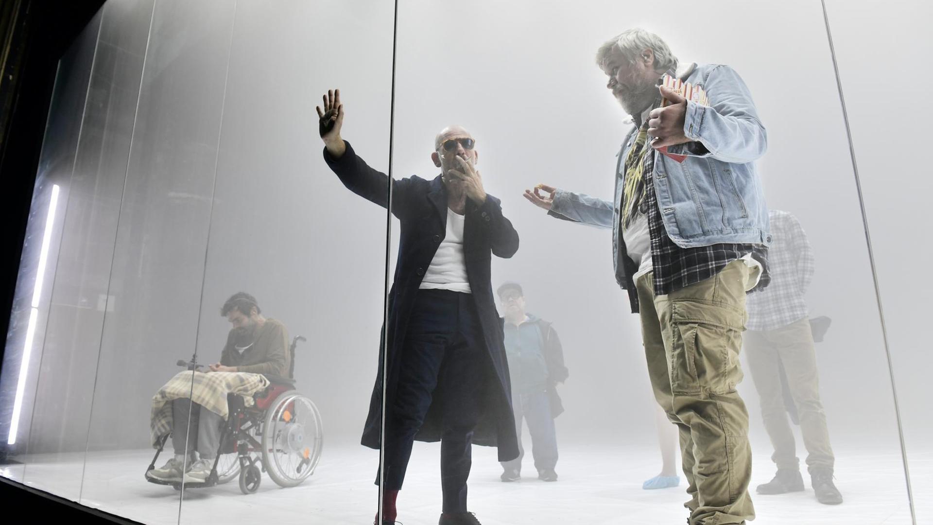 Mehrere Schauspieler stehen hinter einer Glasscheibe, die die Bühne vom Zuschauerraum trennt Mehrere Schauspieler stehen hinter einer Glasscheibe, die die Bühne vom Zuschauerraum trennt