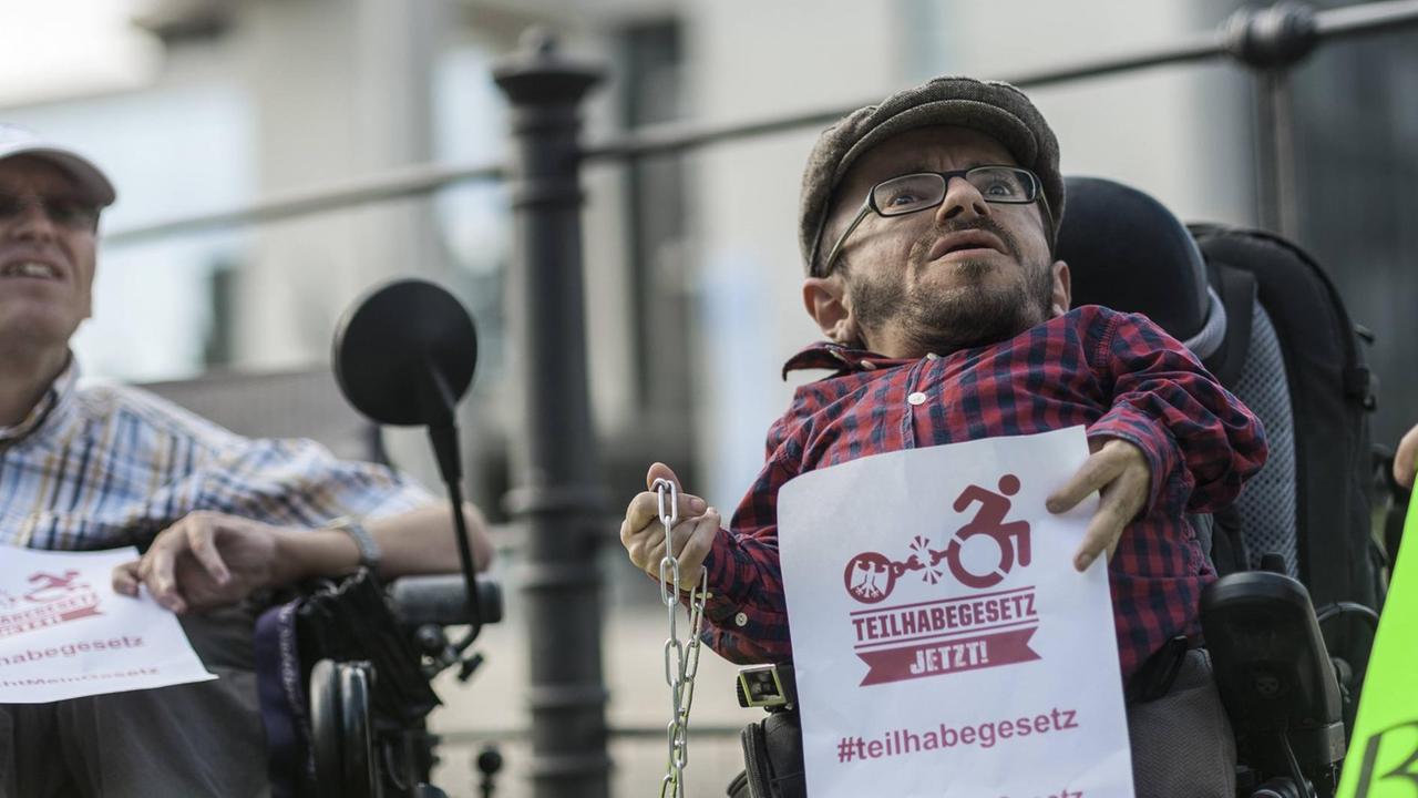 Der Aktivist Raul Krauthausen bei einer Protestaktion gegen das Bundesteilhabegesetz: Er sitzt in einem Rollstuhl, hält einen Zettel mit der Aufschrift "Teilhabegesetz jetzt" in der einen Hand, eine Kette in der anderen. Der Aktivist Raul Krauthausen bei einer Protestaktion gegen das Bundesteilhabegesetz: Er sitzt in einem Rollstuhl, hält einen Zettel mit der Aufschrift "Teilhabegesetz jetzt" in der einen Hand, eine Kette in der anderen.