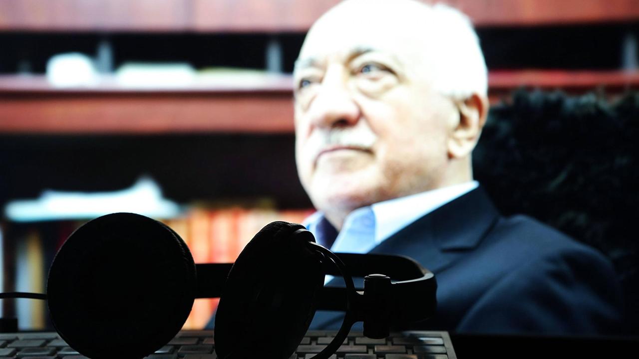 Fetullah Gülen ist auf einem Computerbildschirm zu sehen, davor liegen Kopfhörer und eine Tastatur.
