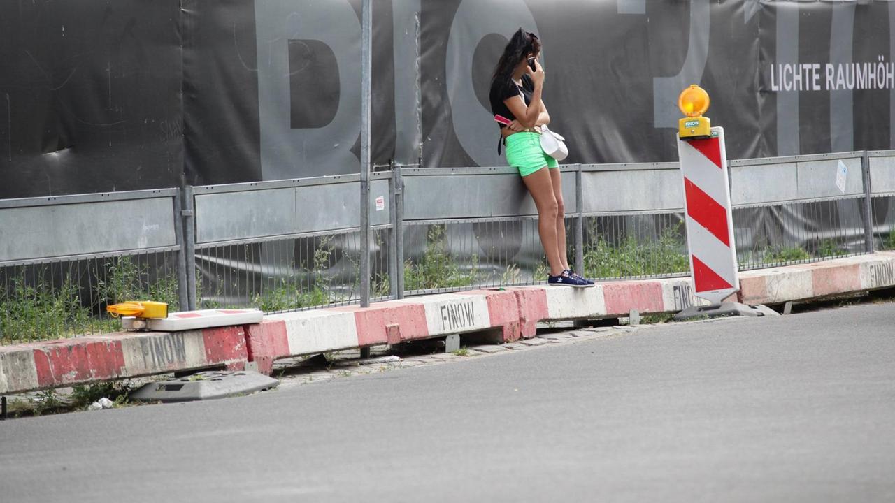 Eine Prostituierte leht sich, mit dem Smartphone in der Hand, an einen Bauzaun in der Kurfürstenstraße, Berlin Eine Prostituierte leht sich, mit dem Smartphone in der Hand, an einen Bauzaun in der Kurfürstenstraße, Berlin