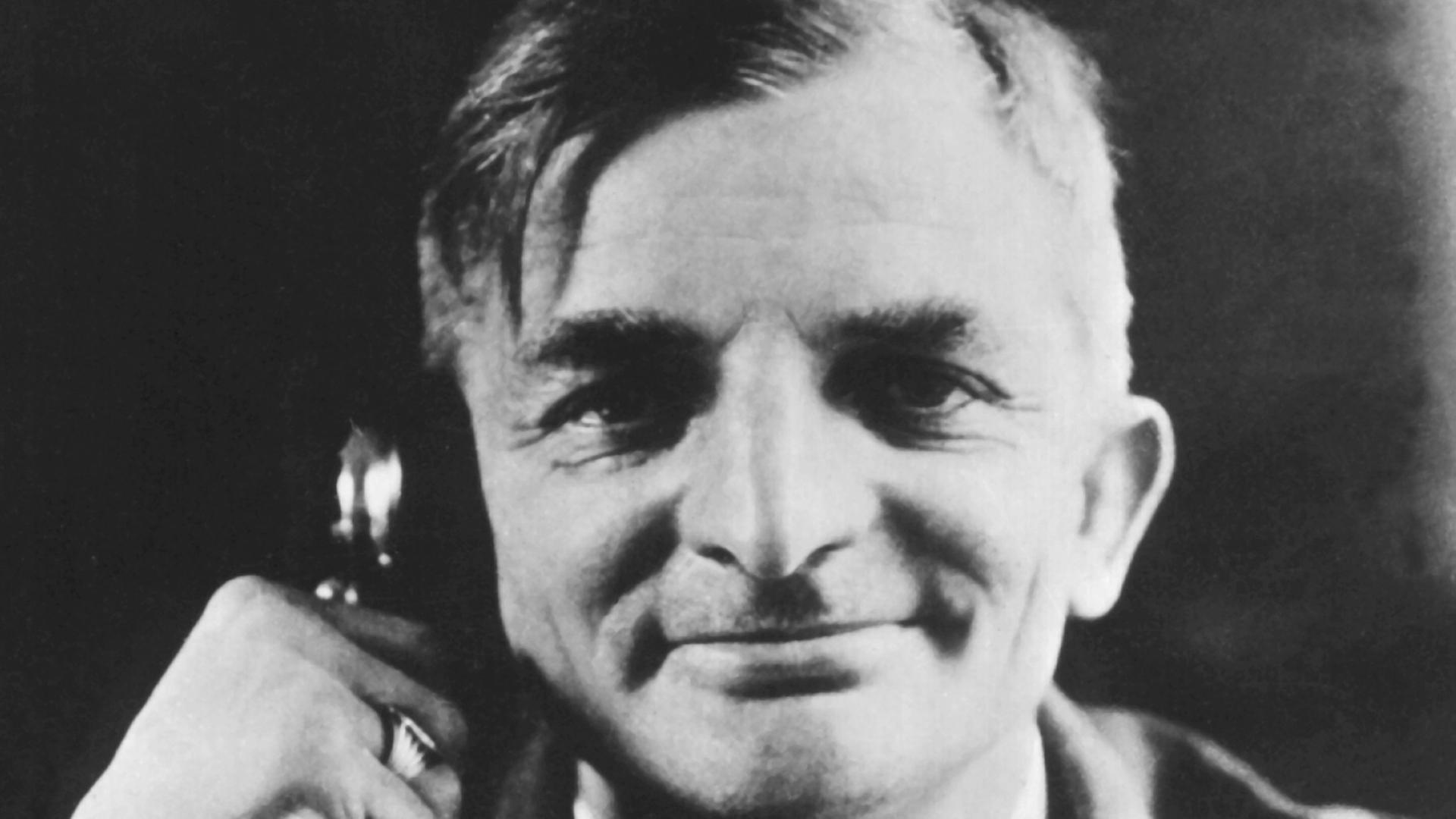 Der Dichter Joachim Ringelnatz mit dem Ohr an einem altmodischen Telefonapparat, den Zuschauer anlächelnd. Der Dichter Joachim Ringelnatz mit dem Ohr an einem altmodischen Telefonapparat, den Zuschauer anlächelnd.