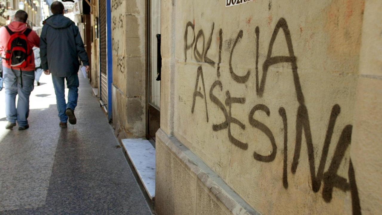 Passanten laufen in San Sebastian im Baskenland an einer Wand vorbei, auf die die Worte "Polizei" und "Mörder" gesprüht wurden