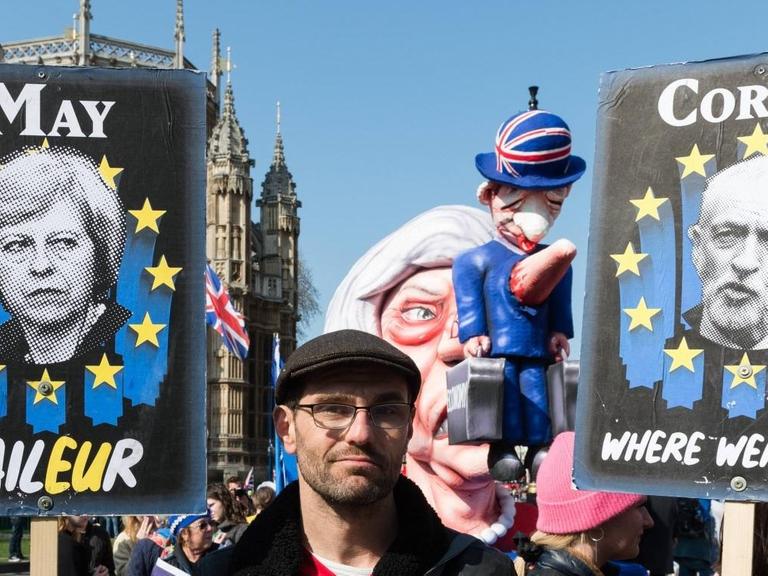 Ein Anti-Brexit-Demonstrant hält Plakate von May und Corbyn in den Händen