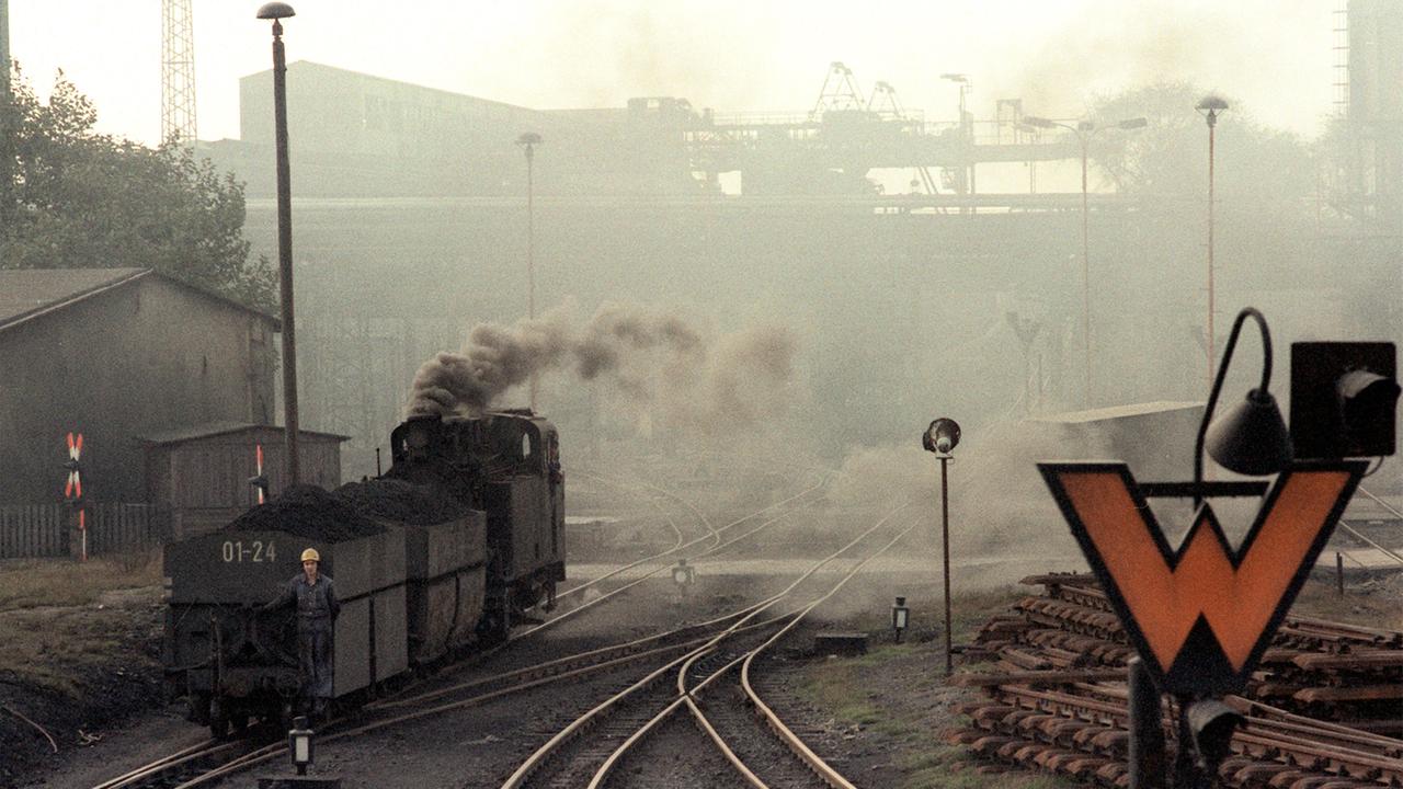 Zu sehen ist eine Werksbahn in einer mit Rauch und Dunst überzogenen Industrieanlage im Mansfeld Kombinat in Hettstedt im Mansfelder Land (Archivbild von 1983).